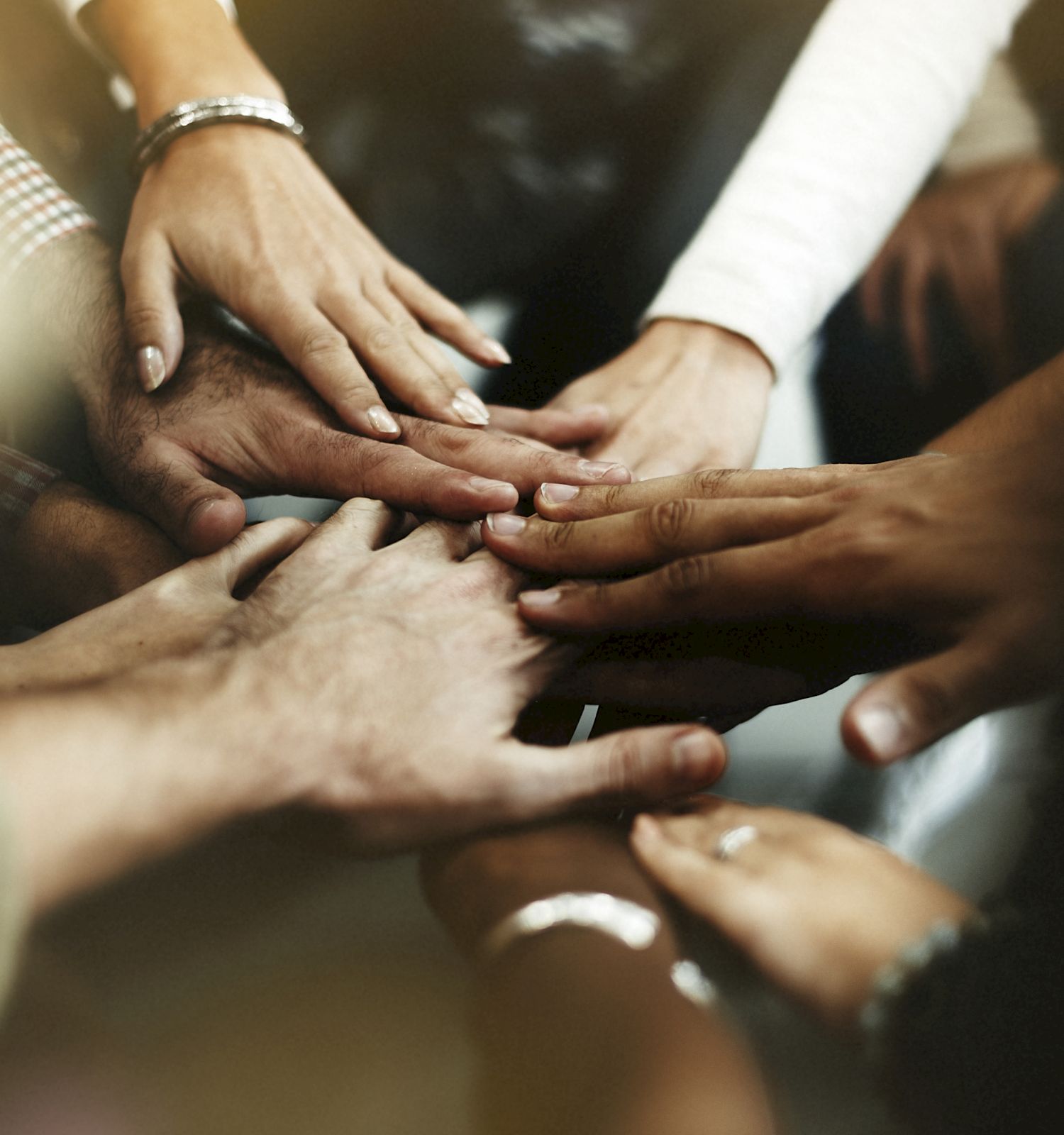 A group of people placing their hands together in a show of unity and teamwork, with various skin tones visible in the image.