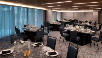 The image shows an elegantly set dining area with round tables, chairs, and dim lighting, prepared for an event or banquet with table settings and decorations.
