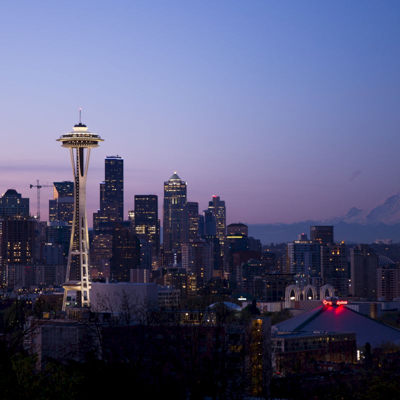 The image depicts the Seattle skyline at dusk, highlighting the Space Needle and downtown buildings with Mount Rainier visible in the background.