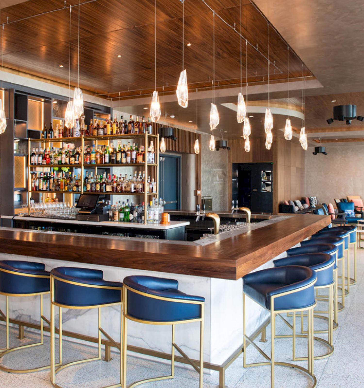 This image features a modern, stylish bar with a well-stocked liquor display, blue bar stools, hanging lights, and a spacious lounge area.