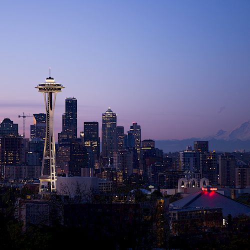 This image shows a city skyline at dusk with the Space Needle prominently in the foreground and Mount Rainier visible in the background.